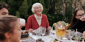 Smiling elderly woman with family and friends enjoying dinner at table backyard garden