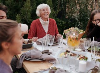 Smiling elderly woman with family and friends enjoying dinner at table backyard garden