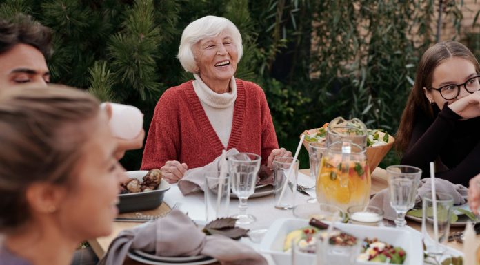 Smiling elderly woman with family and friends enjoying dinner at table backyard garden