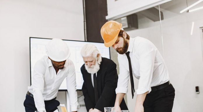 Group of architects discussing construction blueprints wearing hardhats in a modern office.