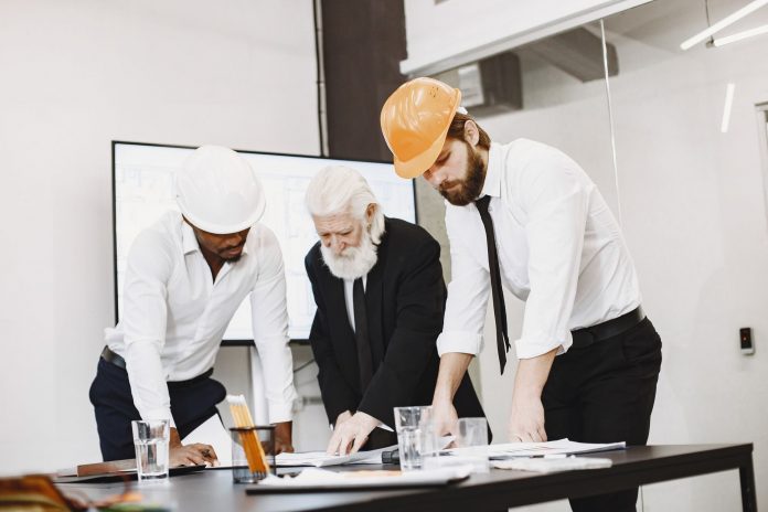 bayonne-mayor-pledges-business-focused-master-plan Group of architects discussing construction blueprints wearing hardhats in a modern office.