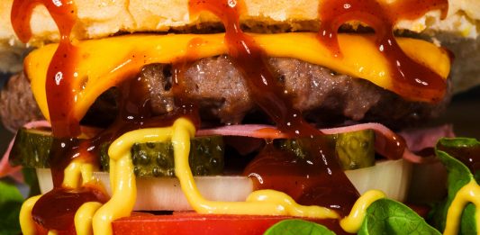 Mouth-watering close-up of a cheeseburger with toppings, showcasing textures and rich flavors.