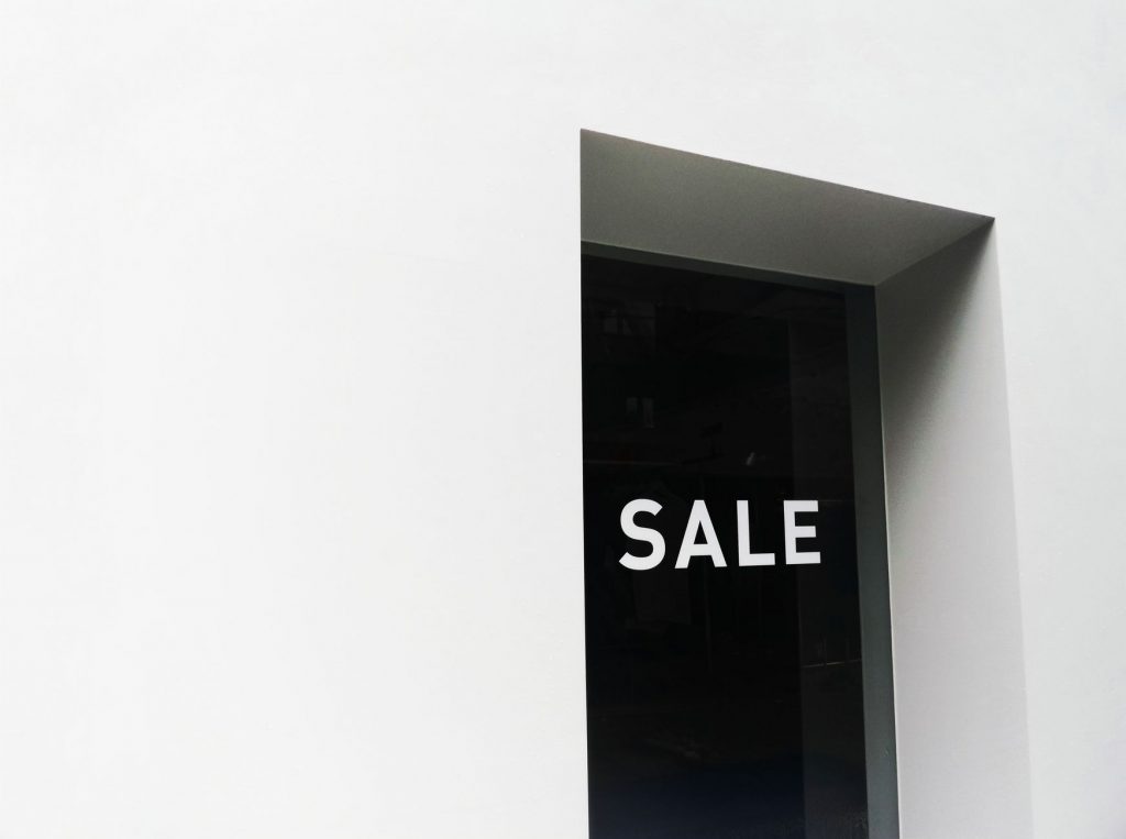 A minimalist black and white image of a sale sign on a store window with ample negative space.