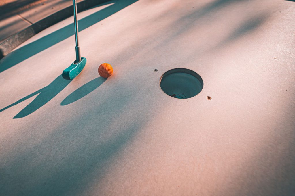 Close-up shot of a mini golf putter and ball near the hole on a sunny day.