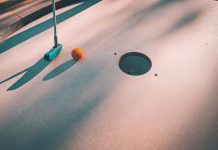 Close-up shot of a mini golf putter and ball near the hole on a sunny day.