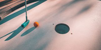 Close-up shot of a mini golf putter and ball near the hole on a sunny day.