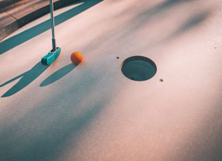 BREAKING: Discover Mini Golf Courses Near Jersey City Close-up shot of a mini golf putter and ball near the hole on a sunny day.