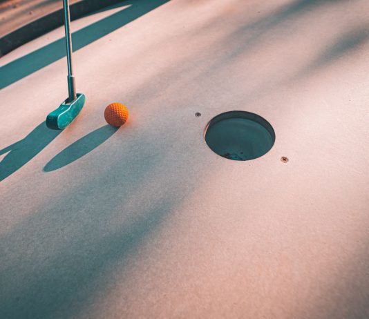 Close-up shot of a mini golf putter and ball near the hole on a sunny day.