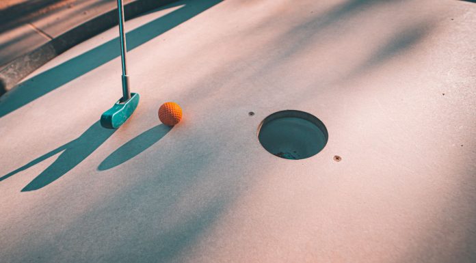BREAKING: Discover Mini Golf Courses Near Jersey City Close-up shot of a mini golf putter and ball near the hole on a sunny day.