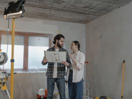 A couple reviews a blueprint in a partially renovated room, planning home improvements.