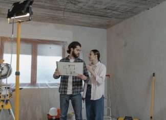 A couple reviews a blueprint in a partially renovated room, planning home improvements.