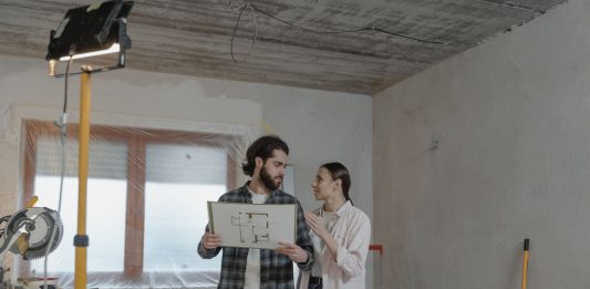 BREAKING: Heights Building Gets City Approval for Full Renovation A couple reviews a blueprint in a partially renovated room, planning home improvements.