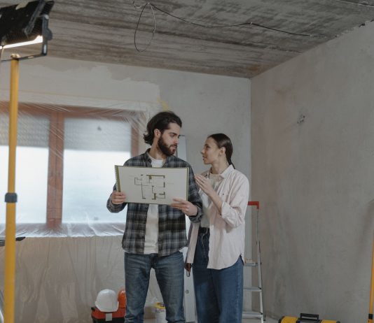 A couple reviews a blueprint in a partially renovated room, planning home improvements.