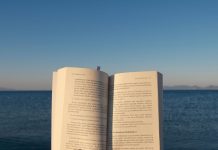 BREAKING: Hoboken Girl Goes on Summer Break Until July 13 An open book is held by the ocean under the calming sunset sky.