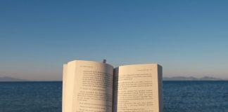 An open book is held by the ocean under the calming sunset sky.