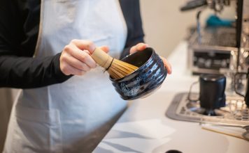 Close-up of a person preparing matcha tea using a bamboo whisk and bowl indoors.