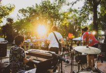 Musicians performing live at a summer outdoor concert during sunset in a park.