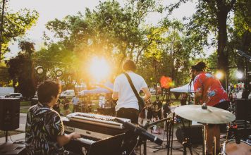 Musicians performing live at a summer outdoor concert during sunset in a park.