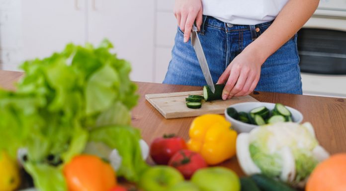 Woman slicing cucumbers surrounded by fresh produce in a bright kitchen setting.