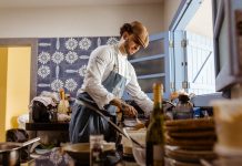 A chef in a rustic kitchen cooks a gourmet meal with an open door filling the room with natural light.
