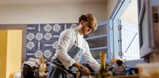 A chef in a rustic kitchen cooks a gourmet meal with an open door filling the room with natural light.