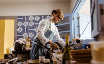 A chef in a rustic kitchen cooks a gourmet meal with an open door filling the room with natural light.