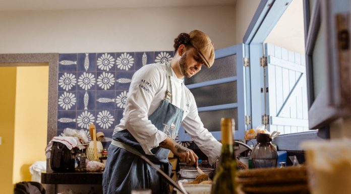 A chef in a rustic kitchen cooks a gourmet meal with an open door filling the room with natural light.
