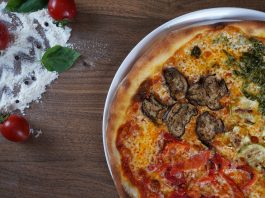 Close-up of homemade pizza with fresh vegetables and herbs on a wooden table.