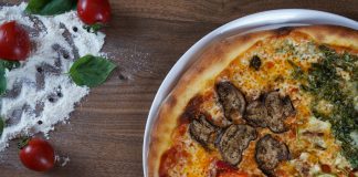 Close-up of homemade pizza with fresh vegetables and herbs on a wooden table.
