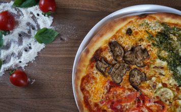 BREAKING: New Weekly Recipe Series Launches for Hudson County Close-up of homemade pizza with fresh vegetables and herbs on a wooden table.