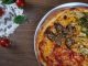 Close-up of homemade pizza with fresh vegetables and herbs on a wooden table.