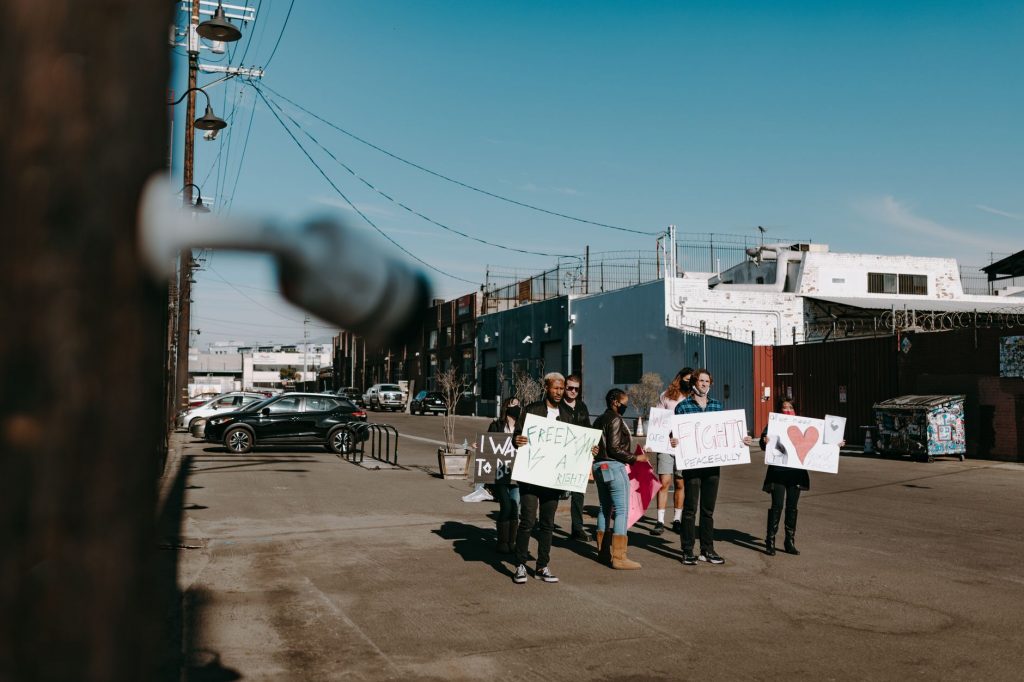 A group of diverse protesters peacefully demonstrating with signs in an open urban space.