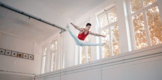 Young sportsman in sportswear doing split in air while jumping on trampoline in gym