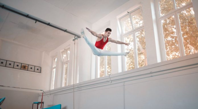 Young sportsman in sportswear doing split in air while jumping on trampoline in gym