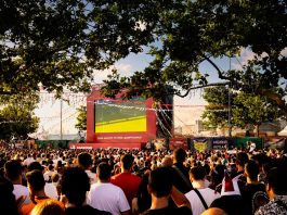 Crowd gathered in İstanbul park watching Euro football on big screen. Energetic summer atmosphere.