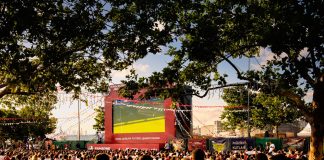 Crowd gathered in İstanbul park watching Euro football on big screen. Energetic summer atmosphere.