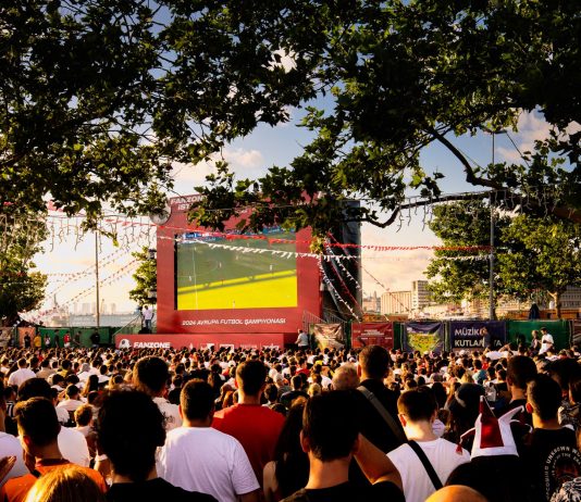Crowd gathered in İstanbul park watching Euro football on big screen. Energetic summer atmosphere.