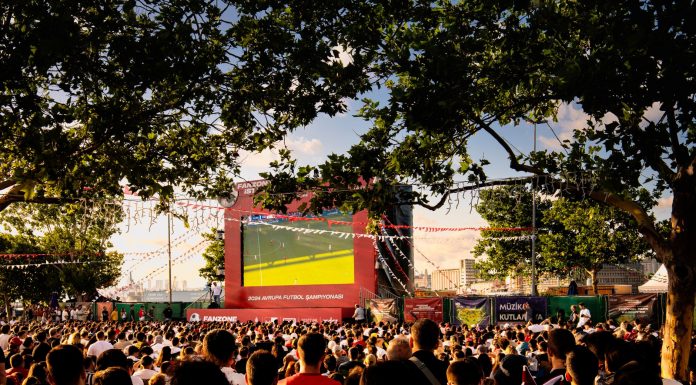 Crowd gathered in İstanbul park watching Euro football on big screen. Energetic summer atmosphere.