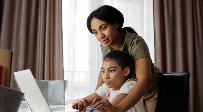 A mother helps her daughter with an online lesson on a laptop, showcasing family bonding and education at home.