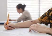 Close-up of student's hands writing on exam sheet, indoors with blurred background.
