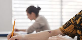 Close-up of student's hands writing on exam sheet, indoors with blurred background.