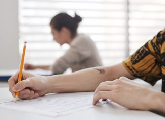 Close-up of student's hands writing on exam sheet, indoors with blurred background.