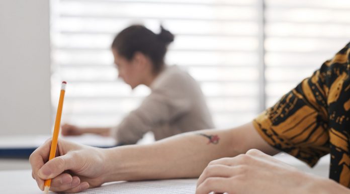 Close-up of student's hands writing on exam sheet, indoors with blurred background.