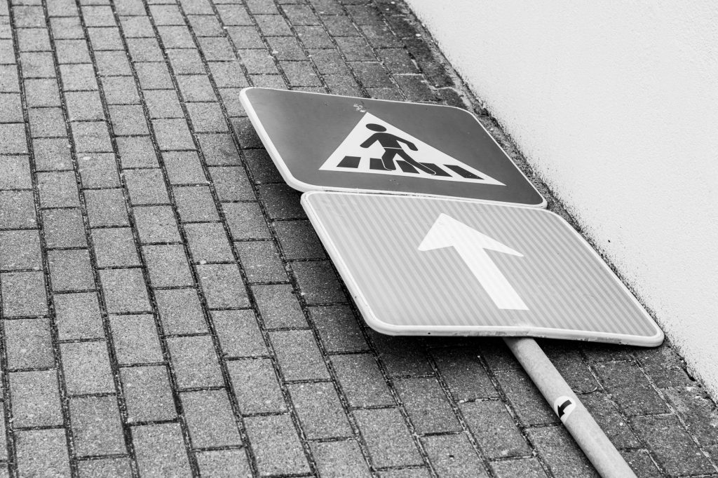 Black and white photo of a fallen street sign on a brick sidewalk.