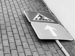 Black and white photo of a fallen street sign on a brick sidewalk.