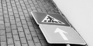 Black and white photo of a fallen street sign on a brick sidewalk.