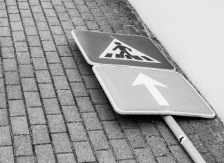 Black and white photo of a fallen street sign on a brick sidewalk.
