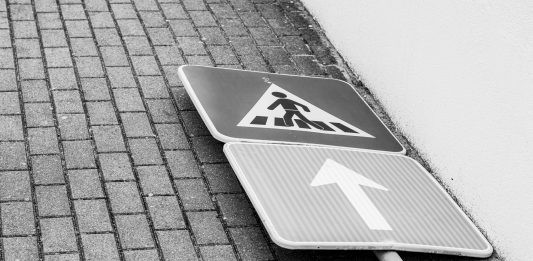 Black and white photo of a fallen street sign on a brick sidewalk.