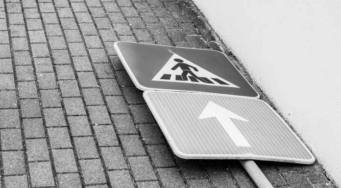 Black and white photo of a fallen street sign on a brick sidewalk.