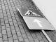 Black and white photo of a fallen street sign on a brick sidewalk.
